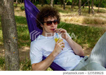 A young guy with curly hair is relaxing on a hammock on a hot summer day. 123589628