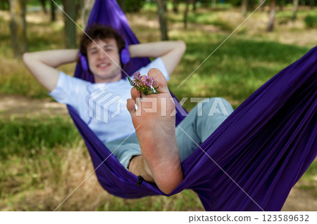 A young guy with curly hair is relaxing on a hammock on a hot summer day. 123589632