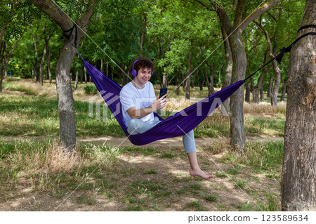 A young guy with curly hair is relaxing on a hammock on a hot summer day. A young guy with curly hair is relaxing on a hammock on a hot summer day. 123589634
