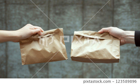 Two hands exchange brown paper bags against a textured wall. Concept of trade or exchange. 123589896
