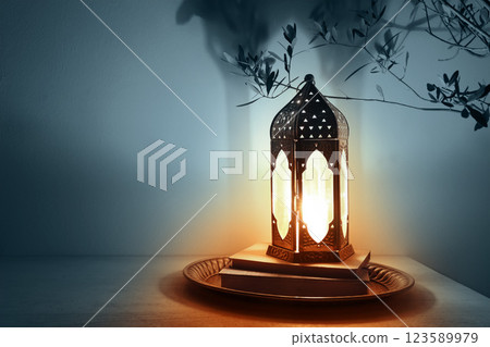 Moroccan, Arabic lantern on table glowing at night. Dark blue background. Silhouette of olive tree branches. Greeting card for Muslim holy month Ramadan Kareem, Eid Mubarak. Festive background. Moroccan, Arabic lantern on table glowing at night. Dark blue background. Silhouette of olive tree branches. Greeting card for Muslim holy month Ramadan Kareem, Eid Mubarak. Festive background. 123589979