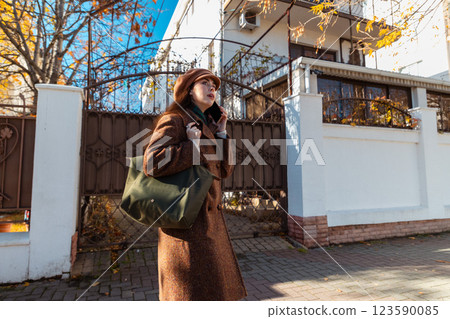 Mid shot of a Caucasian beautiful young woman in a coat and beret, calling on a smartphone on the street. Bottom view. City lifestyle Mid shot of a Caucasian beautiful young woman in a coat and beret, calling on a smartphone on the street. Bottom view. City lifestyle 123590085