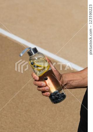 Reusable sport glass bottle with lemon and berry or isotonic in athlete hand. Concept detox, drinking water. Daily water tracker. Water balance for workout. Reusable sport glass bottle with lemon and berry or isotonic in athlete hand. Concept detox, drinking water. Daily water tracker. Water balance for workout. 123590223