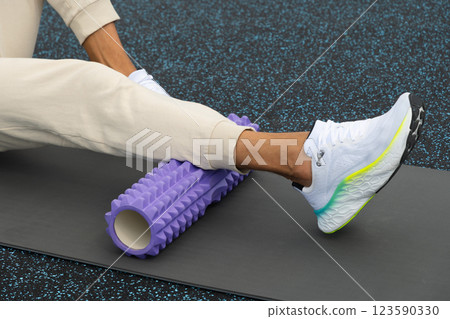 Athlete man exercising and stretching legs on massage roll on sports ground. Outdoor activity. Morning routine. Close up 123590330