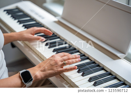 Closeup woman's hand playing piano. Concept of home lesson of music: learning music enhances motor skills, hearing, and intelligence, fostering creativity Closeup woman's hand playing piano. Concept of home lesson of music: learning music enhances motor skills, hearing, and intelligence, fostering creativity 123590712
