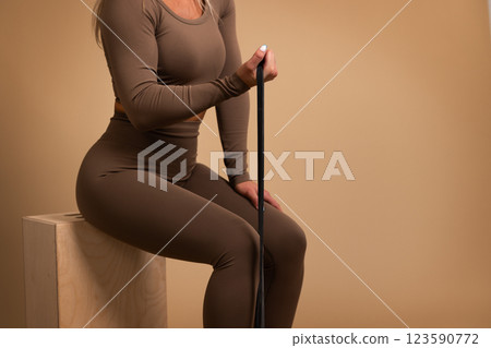 Woman in activewear holding a fitness band seated on a wooden block Woman in activewear holding a fitness band seated on a wooden block 123590772