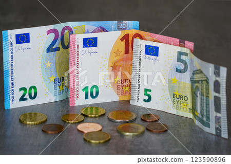 Five, ten and twenty euro banknotes and scattered coins on a gray background, low income concept Five, ten and twenty euro banknotes and scattered coins on a gray background, low income concept 123590896