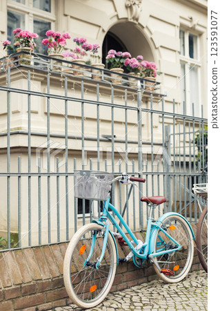 Scenic view turquoise classic retro bicycle parked at fence outside classic urban german house building with pink geraniums pots on balcony. Serene city scene peaceful charm Potsdam lifestyle Scenic view turquoise classic retro bicycle parked at fence outside classic urban german house building with pink geraniums pots on balcony. Serene city scene peaceful charm Potsdam lifestyle 123591077