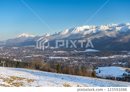 Stunning winter landscape of Zakopane, Poland, featuring the snow-covered Tatra Mountains at sunset. The picturesque alpine town, surrounded by forests and peaks, offers breathtaking views and is a po 123591086