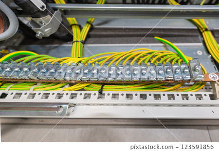 Grounding busbar with connected yellow-green wires inside an industrial electrical cabinet 123591856