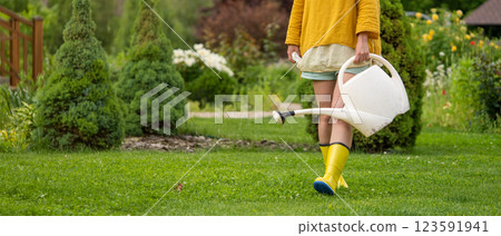 A professional woman gardener with a watering can is irrigating her lawn and flowers. A professional woman gardener with a watering can is irrigating her lawn and flowers. 123591941