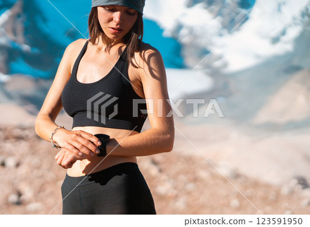 Girl looks at her watch, snowy mountains on the backdrop. Girl looks at her watch, snowy mountains on the backdrop. 123591950