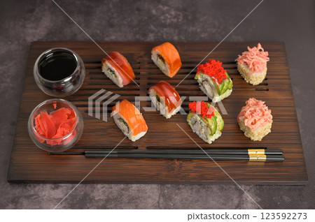 Set of sushi roll with rice and fish, soy sauce and ginger into a glass bowl, chopsticks on wooden serving board. Dark black texture background with copy space. Japan menu. Asian food 123592273