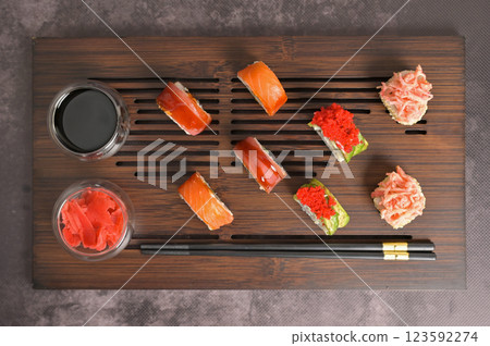 Set of sushi roll with rice and fish, soy sauce and ginger into a glass bowl, chopsticks on wooden serving board. Top view. Dark black texture background. Japan menu. Asian food 123592274