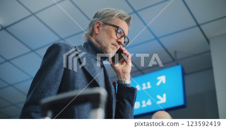 Crowded International Airport Terminal: Mature Man Holding Plane Ticket, Talking by Mobile Phone 123592419