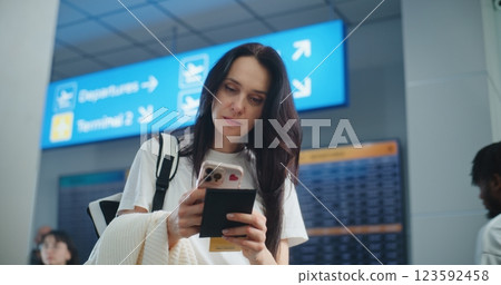 Crowded Airport Terminal: Woman Scanning Plane Ticket Using Phone to Check Flight Information Crowded Airport Terminal: Woman Scanning Plane Ticket Using Phone to Check Flight Information 123592458