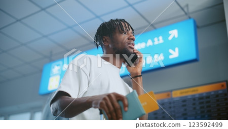 Airport Terminal: Man Talking by Phone, Checking Flight Information on Arrival and Departure Display 123592499