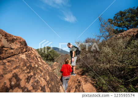 Father and daughter hiking in rocky mountain terrain under clear blue sky Father and daughter hiking in rocky mountain terrain under clear blue sky 123593574