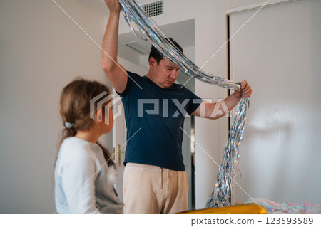 Caucasian adult male and child preparing party decorations with streamers indoors Caucasian adult male and child preparing party decorations with streamers indoors 123593589