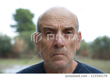 Serious Elderly Bald Man Looks Around Seated in Nature Park 123594176