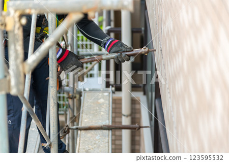[Large-scale apartment building repair work: Workers connecting wall ties and building scaffolding] 123595532