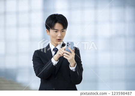 A young man in a business suit looking at his smartphone A young man in a business suit looking at his smartphone 123598487