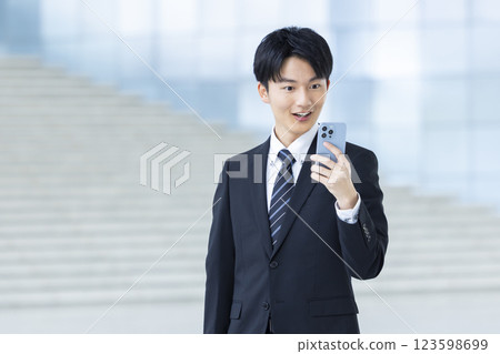 A young man in a business suit looking at his smartphone 123598699