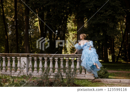 Romantic Woman in a Light Blue Gown Posing on a stone balustrade in a picturesque garden. Romantic Woman in a Light Blue Gown Posing on a stone balustrade in a picturesque garden. 123599116