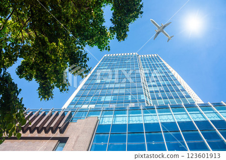 A modern office skyscraper and white passenger airplane flying over this building A modern office skyscraper and white passenger airplane flying over this building 123601913