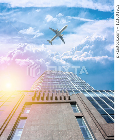 A modern office skyscraper in the morning sun and a white passenger airplane flying over this building 123601915