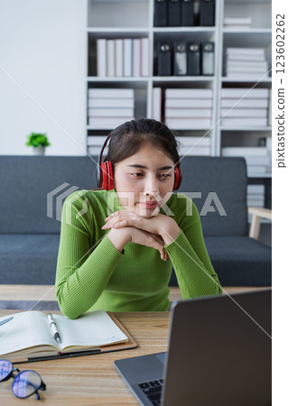Woman sitting at a table using laptop in a brightly lit room while engaged in work or personal projects at home 123602262