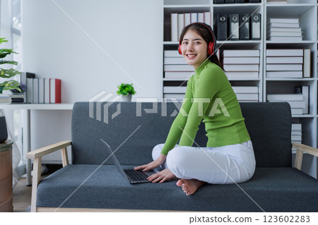 Woman relaxing on couch wear headphones, listening to music while using computer in cozy home Woman relaxing on couch wear headphones, listening to music while using computer in cozy home 123602283