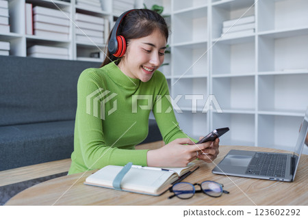 Woman sitting comfortably at a table with a laptop and smartphone enjoying music and relaxation in a cozy home setting Woman sitting comfortably at a table with a laptop and smartphone enjoying music and relaxation in a cozy home setting 123602292