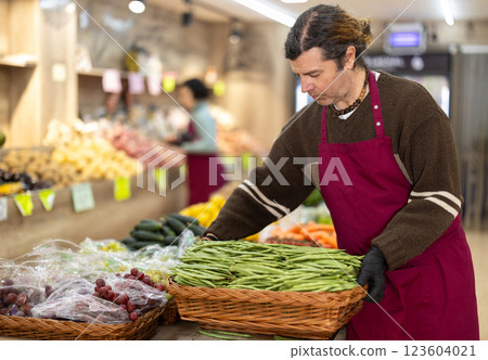 Man salesperson carries large basket of beans in pods from warehouse to sales area in shop 123604021