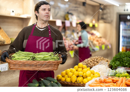 Man salesperson carries large basket of beans in pods from warehouse to sales area in shop 123604086