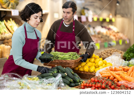 Woman shop seller puts cucumber goods on display case, man assistant in background 123604152