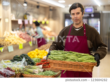 Man salesperson carries large basket of beans in pods from warehouse to sales area in shop 123604282