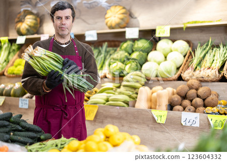 Adult man seller with green onions in vegetable shop 123604332