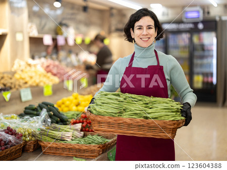 Woman salesperson carries large basket of beans in pods from warehouse to sales area in shop 123604388