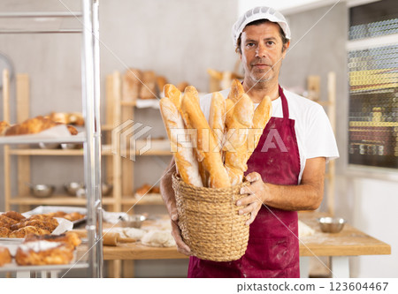 Caucasian male cook-baker worker with basket of baguettes, shows many products Caucasian male cook-baker worker with basket of baguettes, shows many products 123604467