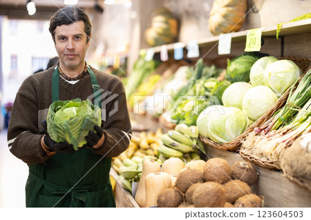 Man store employee offers to buy savoy cabbage, demonstrates product 123604503