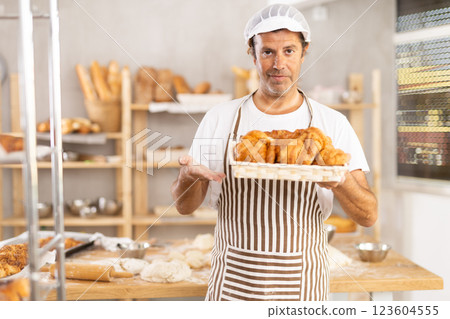Caucasian male cook-baker worker with basket of croissant, shows many products Caucasian male cook-baker worker with basket of croissant, shows many products 123604555