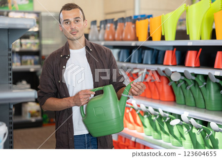 Young man chooses watering can in store Young man chooses watering can in store 123604655