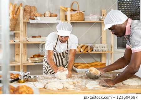 African man and male assistant make dough, employee kneads dough, assistant works with rolling pin 123604687