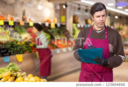 Man store employee with folder of documents takes inventory in vegetable store Man store employee with folder of documents takes inventory in vegetable store 123604698
