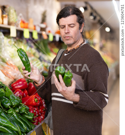 Man carefully selects red bell peppers in grocery supermarket 123604781