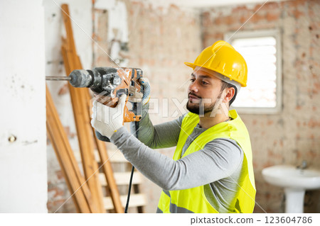 Professional builder drilling hole in wall with perforator in repairable room 123604786