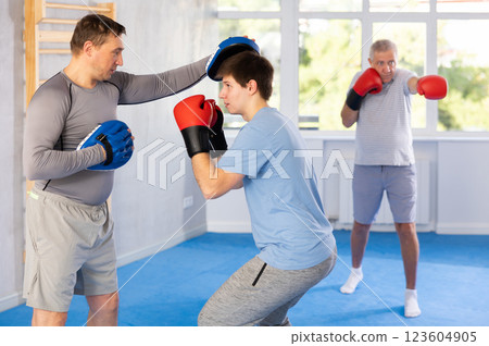 Guy in boxing gloves punching mitts in hands of instructor at self-defense class 123604905