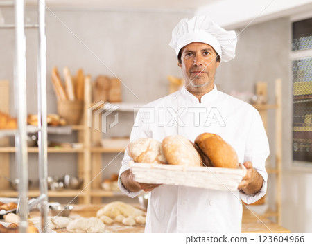 Caucasian male cook-baker worker with loafs of bread, shows many products 123604966