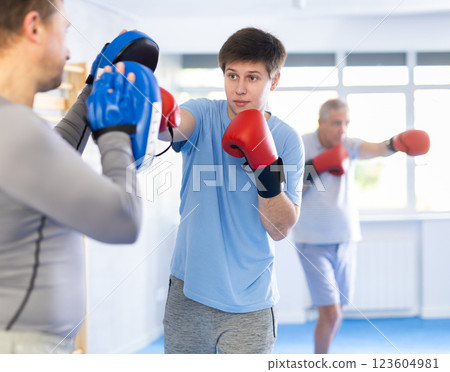 Boxing training - young guy masters boxing strikes on trainer punch mitts during training 123604981